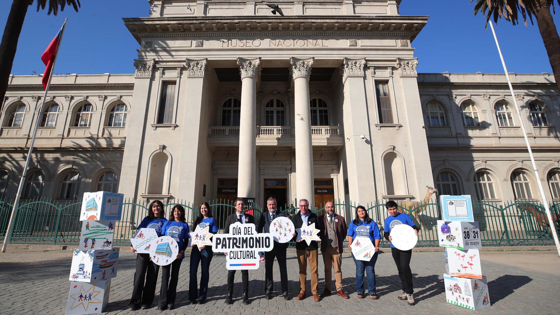Lanzamiento del DPC 2026: Ministro de las Culturas, Subsecretario del Patrimonio, director del MHNH y director de la RM del Serpat, junto a voluntarios, en el frontis de Museo Nacional de Historia Natural, sosteniendo letreros con la gráfica del Día del Patrimonio 2026