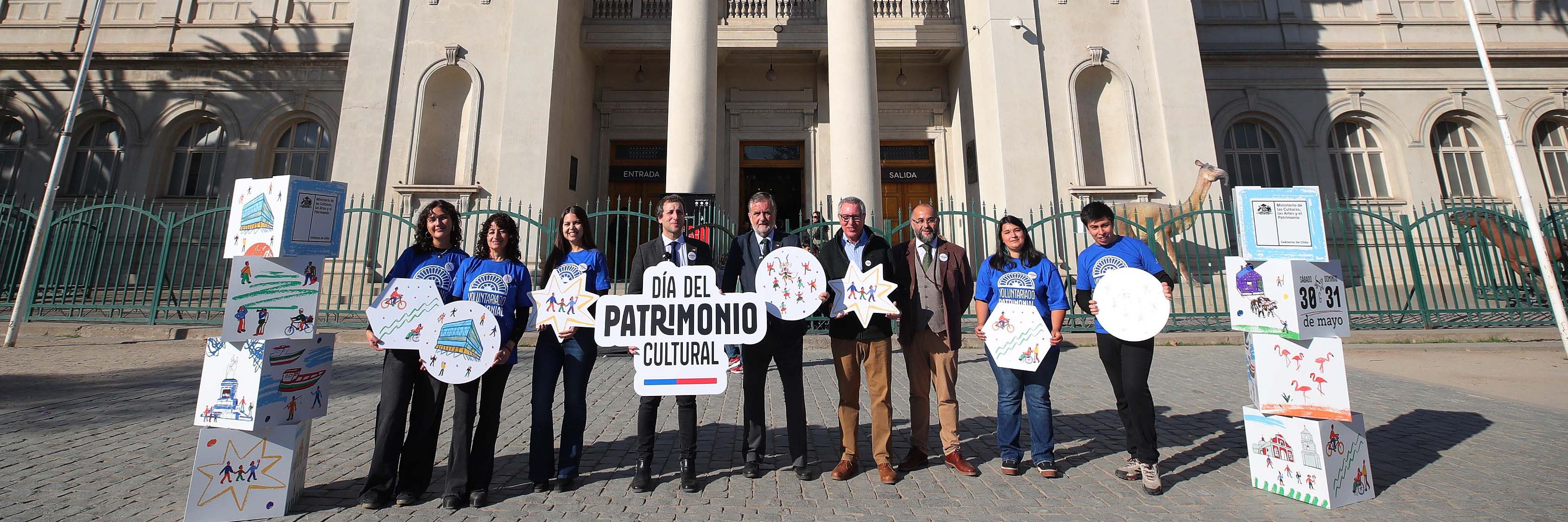 Lanzamiento del DPC 2026: Ministro de las Culturas, Subsecretario del Patrimonio, director del MHNH y director de la RM del Serpat, junto a voluntarios, en el frontis de Museo Nacional de Historia Natural, sosteniendo letreros con la gráfica del Día del Patrimonio 2026